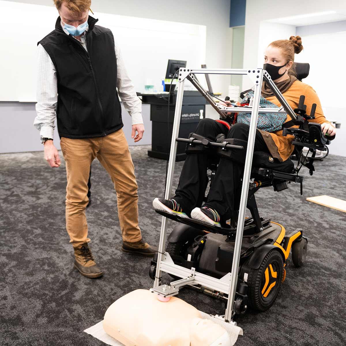 工程 students help a student in a wheelchair use the assistive CPR device, 哪一个使用杠杆动作来增加力量和实现必要的胸部压迫.